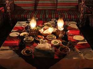 guests enjoying the authentic emirati traditional food along with the belly dancer, fire show, and tanoura folklore performaces with camel rides in dubai desert on a bbq dinner in dubai desert